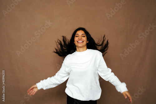 Positive ethnic female in white sweatshirt and with flying hair having fun in studio with closed eyes photo
