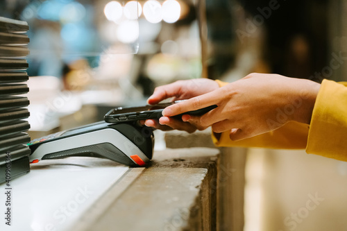 Unrecognizable crop female buyer using smartphone for payment on POS terminal in city