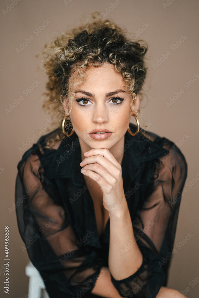 Pensive female in elegant black outfit leaning on hand and looking at camera on brown background Pensive female in elegant black outfit leaning on hand and looking at camera on brown background