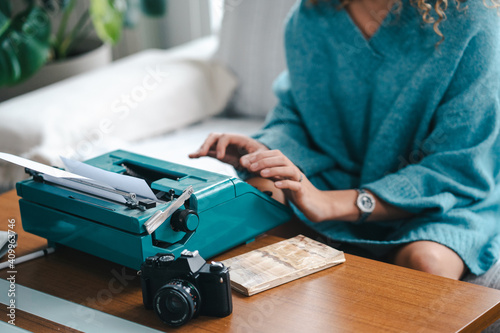 Crop view of anonymous female author sitting on sofa and using vintage typewriter while creating interesting story photo