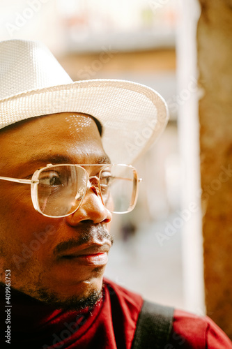 Determined African American male wearing elegant hat and clothes standing in street looking away photo