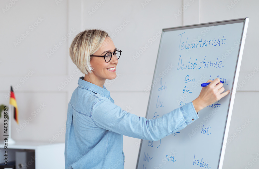 Happy young German tutor writing grammar rules on blackboard, giving online lesson from home Happy young German tutor writing grammar rules on blackboard, giving online lesson from home