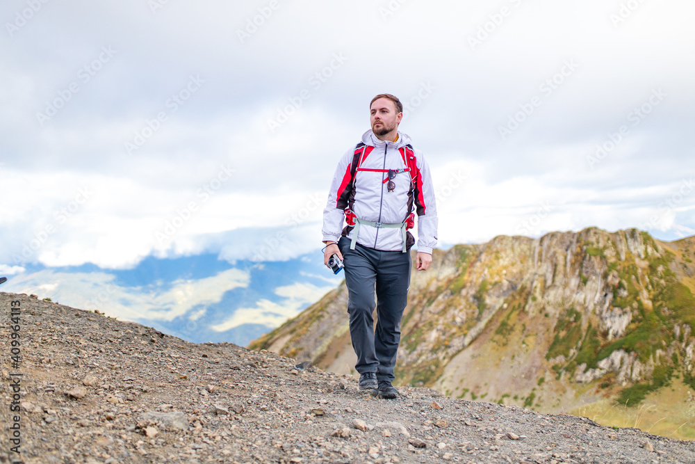 Fototapeta premium Young bearded man wearing white puff jacket standing near a mountain