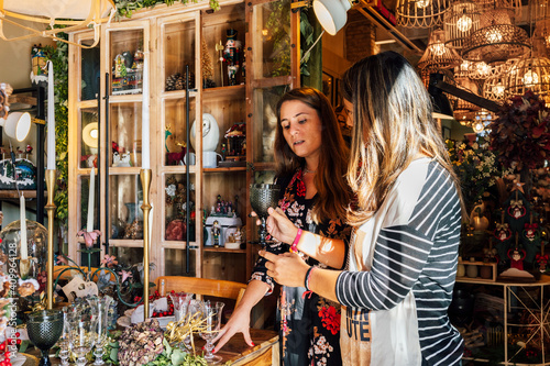 Professional female holding decorative vintage wine glass while helping costumer in decor shop photo