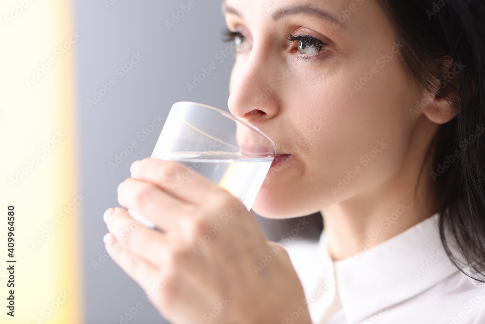 Young woman holding glass in her hands and drinking water from it Young woman holding glass in her hands and drinking water from it