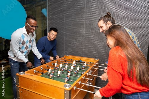 Cheerful young multiethnic people in casual clothes having fun and playing table football together