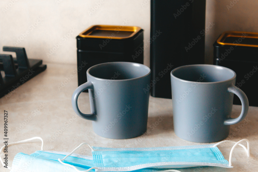 A pair of coffee cups sitting on the table, cogni next two medicinskie masks. A way of life, a new reality. The concept of home comfort and meetings A pair of coffee cups sitting on the table, cogni next two medicinskie masks. A way of life, a new reality. The concept of home comfort and meetings