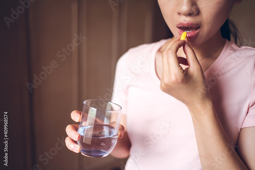 Crop unrecognizable female with glass of fresh water taking yellow vitamin pill while representing healthy lifestyle concept photo