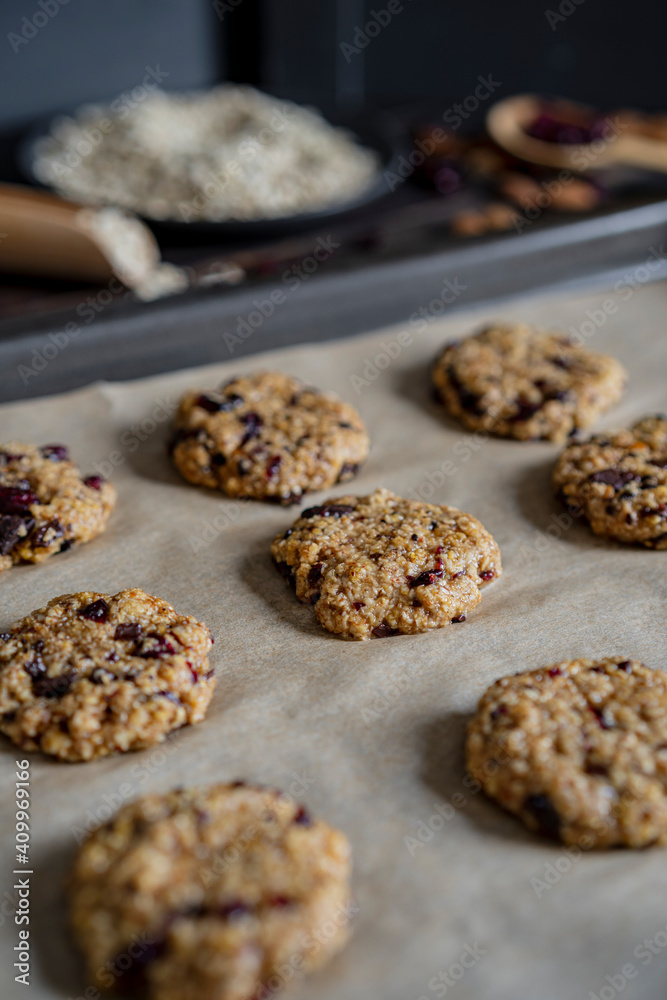 Oatmeal cranberry round cookies before oven, homemade healthy vegan snack or biscuits. Homemade nut bars on baking sheet with ingredients for cooking  on rustic table. Selective focus, copy space