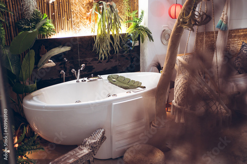 Cozy hotel room with white bathtub and hanging rope chair near green tropical plants in traditional oriental style in Taiwan