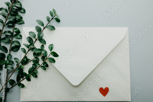 Minimal composition with a white envelope, heart and green leaves