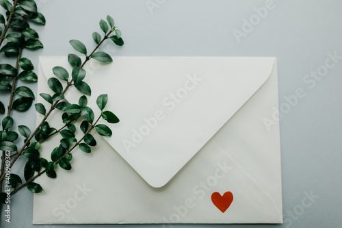 Minimal composition with a white envelope, heart and green leaves