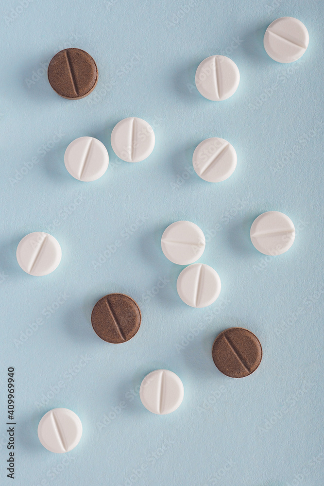 White and brown pills lie on a sheet of blue paper. Close-up. Light vertical background or backdrop on the theme of medicine, health care, drugs, pharmacology. Tablets of different colors. Top view