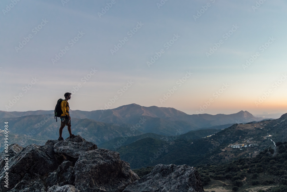 Full body side view of lonely unrecognizable male explorer with backpack standing on top of rough rocky mountain and enjoying freedom while hiking through highlands at sunset Full body side view of lonely unrecognizable male explorer with backpack standing on top of rough rocky mountain and enjoying freedom while hiking through highlands at sunset