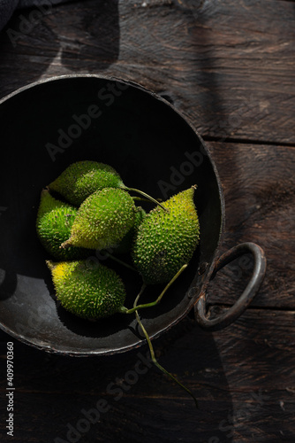 From above of ripe green spiny gourds in bowl placed on rusty wooden table in kitchen photo