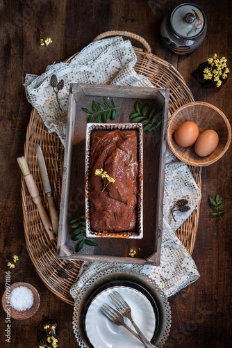 Top view composition with palatable homemade rustic chocolate pound cake in baking dish placed on wooden table with ingredients and cuttlery photo