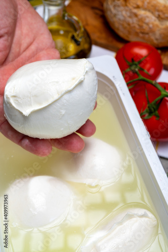 Cheese maker holding in hand fresh handmade soft Italian cheese from Campania, white balls of buffalo mozzarella cheese made from cow milk in container with water #409973963