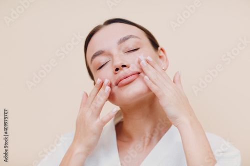 Young woman applying cosmetic white cream on her face