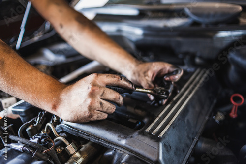 Unrecognizable technician with greasy hands turning screw with spanner while fixing engine of car in garage photo