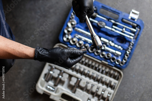 From above anonymous male technician in latex gloves selecting wrench bit from tool box during work in garage