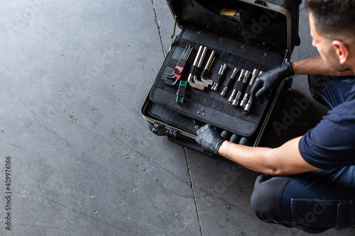 From above male technician picking screwdriver bits from tool box while working in garage photo