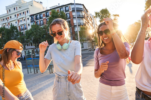Happy carefree teen female friends in trendy clothes and sunglasses having fun and dancing together on urban street while enjoying summer day in city