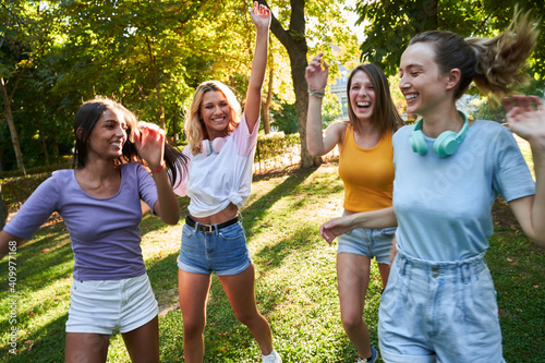 Group of laughing multiracial teen female friends having fun and dancing together while spending summer day in green park photo