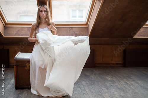 Young romantic elegant girl in long white floating dress sitting on the dower chest in the loft photo