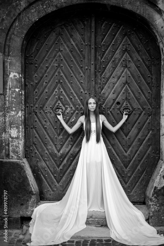 Young romantic elegant girl in long white dress posing over ancient door
