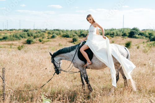 Young romantic elegant girl in long white flowy dress posing on the horse in the countryside © benevolente
