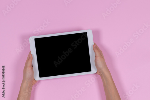 Hands holding digital tablet computer on pastel pink background