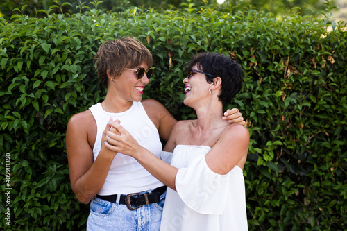 Adult friendly women cuddling in green park while smiling sincerely photo