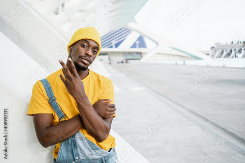 African American male in trendy yellow outfit standing on street and showing rude sexual shocker gesture while looking at camera photo