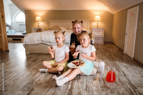 Mother and her daughters watching TV and eating pizza, drinking juice at home photo