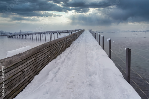 Snow-covered pedestrian wooden bridge (Holzsteg) crossing the Zurich Lake at its narrowest point between Hurden (Seedam) and Rapperswil, Switzerland © Luis