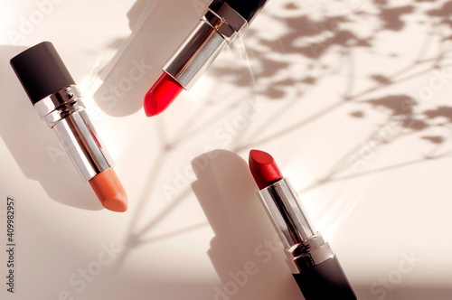Fashion colorful lipsticks sun shadows from flowers on beige background flat lay top view. Beauty and cosmetics background. Decorative cosmetics makeup women's lipstick beauty brand product design photo