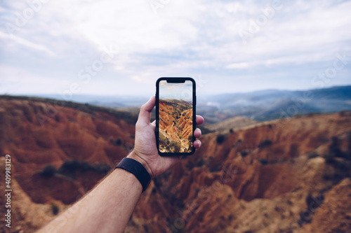Crop unrecognizable male hiker shooting picture of eroded mountainous landscape on mobile phone while travelling through highlands and exploring wild nature
