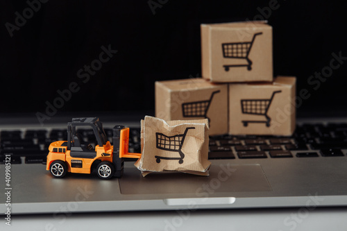Orange forklift model and broken carton box on a keyboard. Courier service and shipment accident concept.