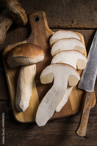 From above composition of raw whole and sliced porcini or cep mushrooms with knife and cutting board on wooden rustic table
