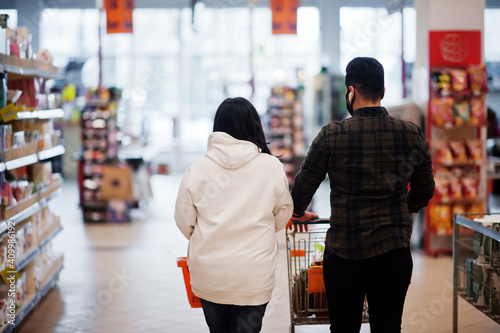 Back view of asian couple wear in protective face mask shopping together in supermarket during pandemic. photo