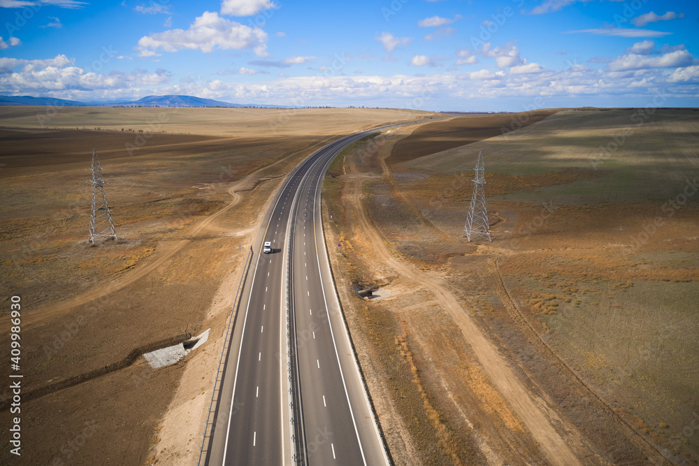 From above drone view of curvy asphalt roadway with lonely car running through desert grassy land in mountainous region in sunny autumn day From above drone view of curvy asphalt roadway with lonely car running through desert grassy land in mountainous region in sunny autumn day