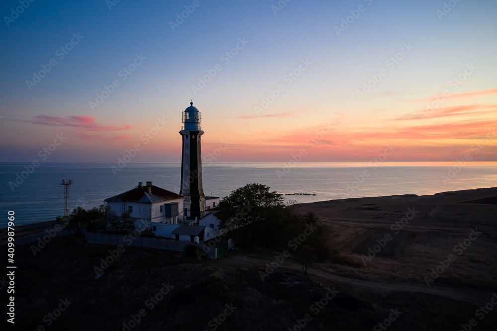 Spectacular drone view of beacon located on hill on background of calm sea and sundown sky