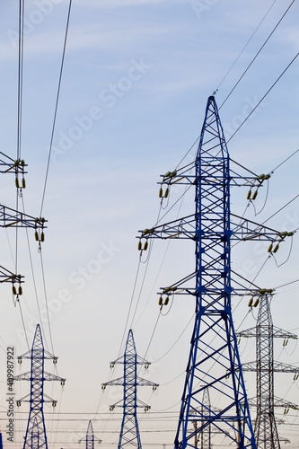 High voltage power lines pylons and electrical cables on a clear blue sky background. Modern infrastructure of high voltage transmission lines. Overhead power lines towers equipment. Energy industry.