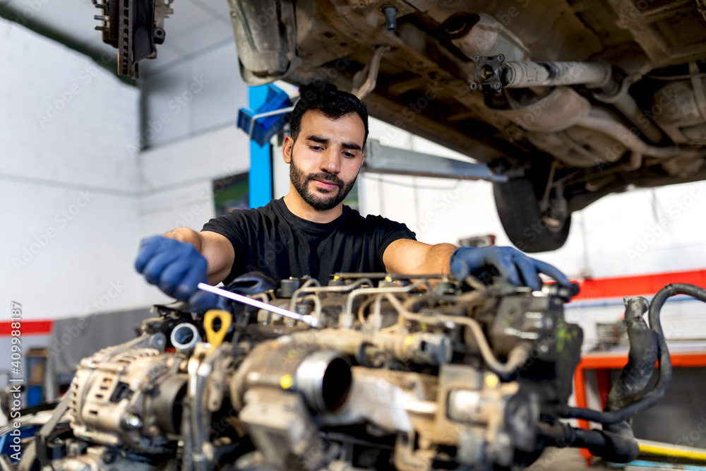 Busy bearded male mechanic with metal wrench repairing dirty car engine in modern service Busy bearded male mechanic with metal wrench repairing dirty car engine in modern service