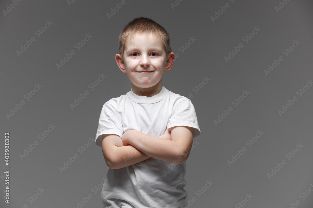 Portrait of happy little boy in white t-shirt smiling on gray background looking at camera in studio setting. Portrait of fashionable male child. Portrait of happy little boy in white t-shirt smiling on gray background looking at camera in studio setting. Portrait of fashionable male child.
