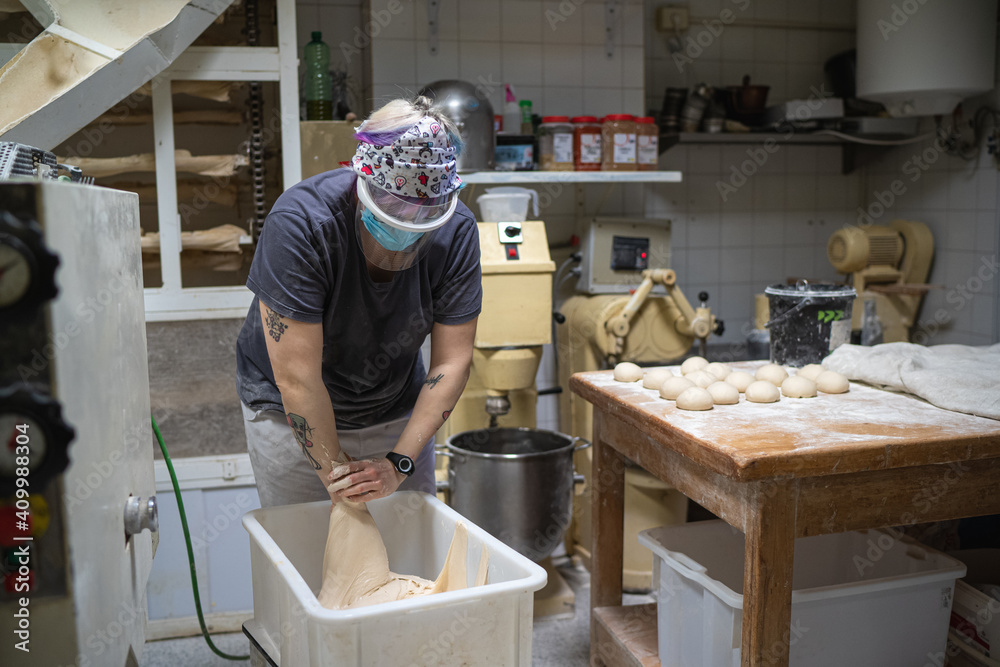 Unrecognizable female baker in mask working in bakery and kneading raw dough while cooking delicious bread Unrecognizable female baker in mask working in bakery and kneading raw dough while cooking delicious bread
