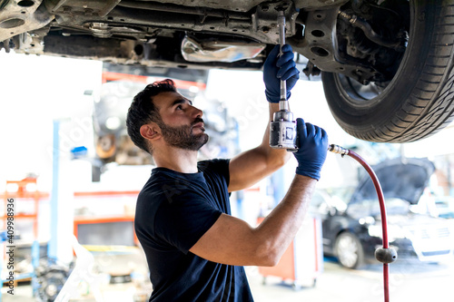 Busy male technician using special instrument and fixing car while working in modern service photo