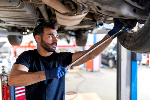 Focused male mechanic with metal wrench screwing detail of car wheel while working in service photo