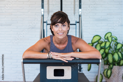 Adult female smiling and looking at camera while relaxing on reformer during break in Pilates training in gym photo