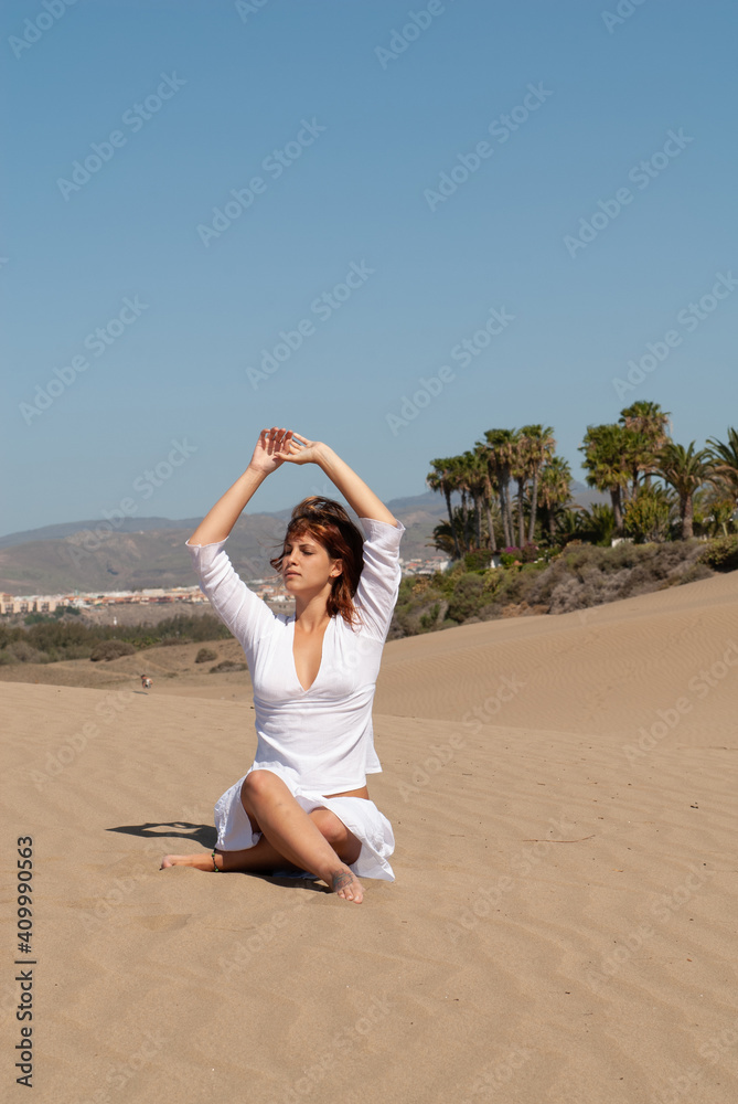 woman dressed in white performing meditation and yoga postures on the sand dunes on sunny day woman dressed in white performing meditation and yoga postures on the sand dunes on sunny day
